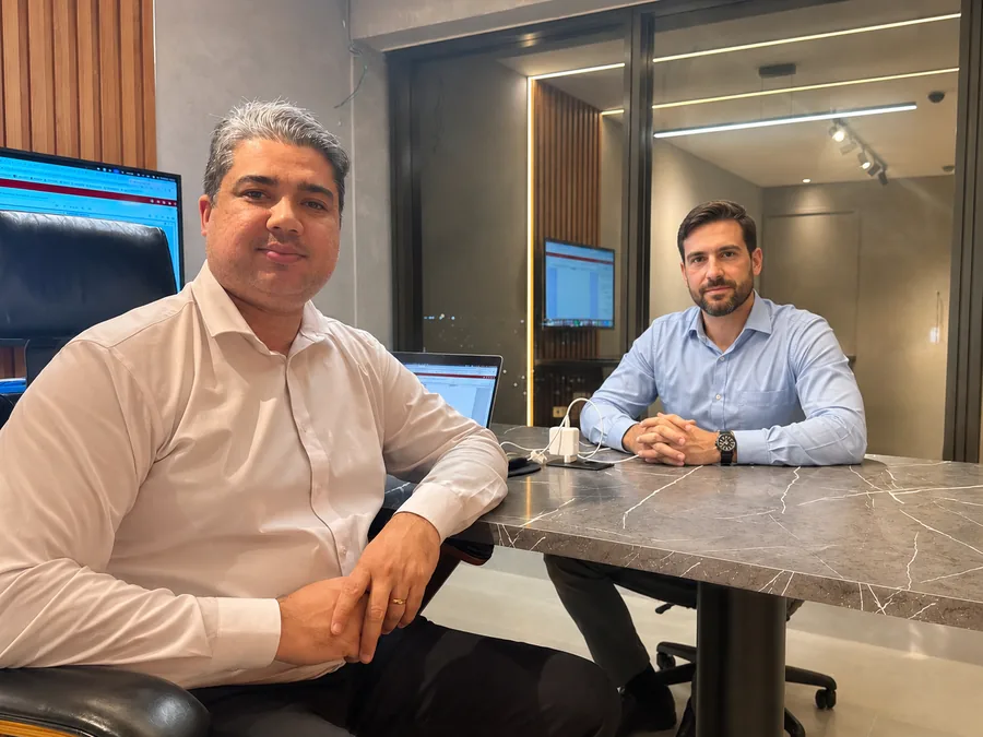 Dr. Capistrano Barros sentado à mesa de reunião do escritório, com outra pessoa à mesa ao fundo